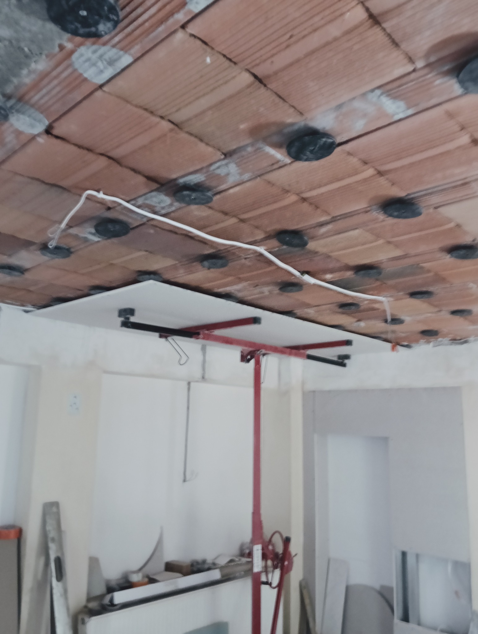 Montaż płyty gipsowej na suficie z użyciem podnośnika. Widoczne elementy konstrukcyjne i instalacja elektryczna. Wnętrze w trakcie prac wykończeniowych.
