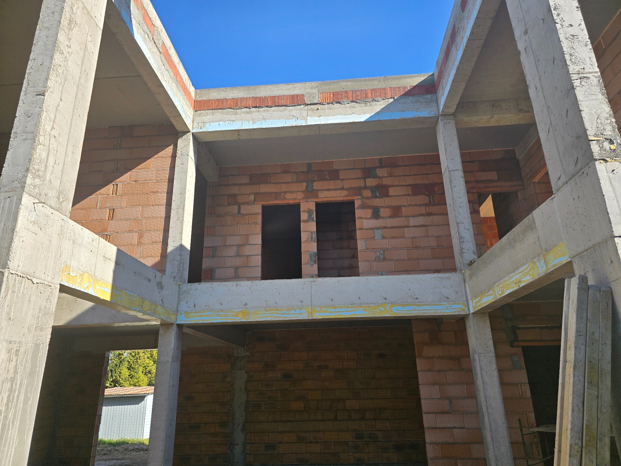 Surowy stan domu murowanego z czerwonej cegły i szkieletu betonowego we Wrocławiu, w trakcie budowy, przy słonecznej pogodzie i błękitnym niebie.