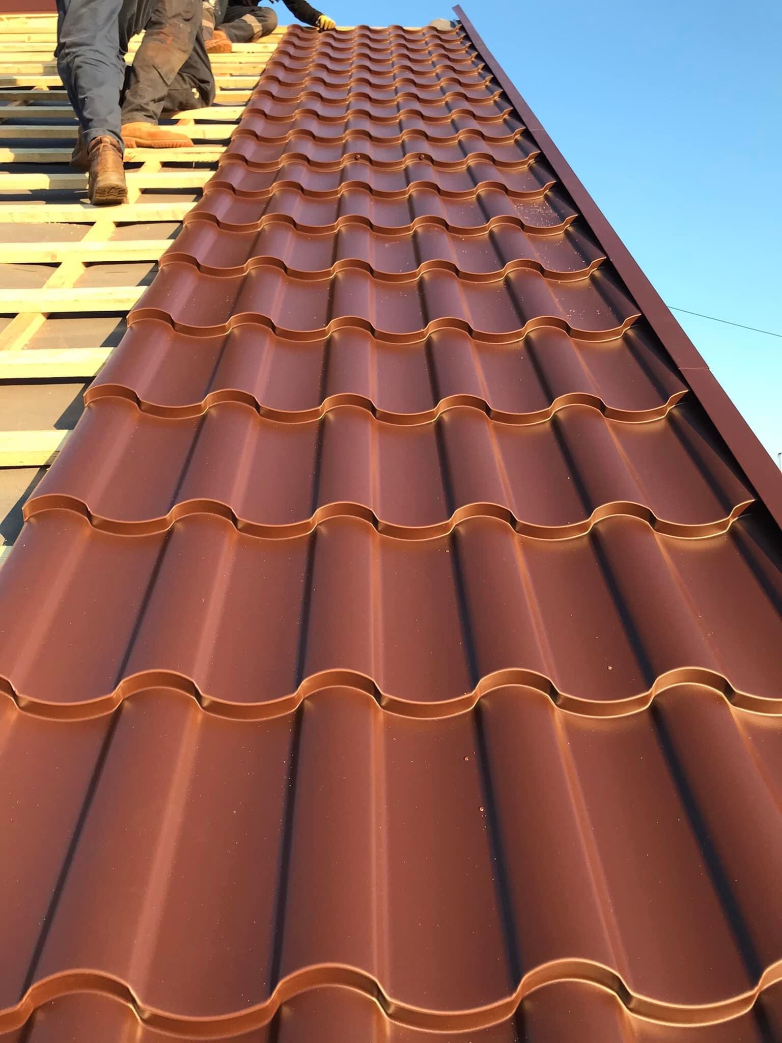 Montaż blachodachówki w kolorze miedzianym na konstrukcji drewnianej dachu, widoczne fragmenty pracowników w odzieży roboczej.