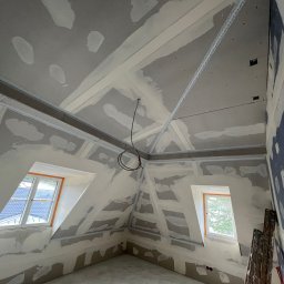 MATEUSZ MOTOR - Poddasze w trakcie prac przygotowawczych do wykończenia, widoczne profile, częściowo nałożona masa szpachlowa na ścianach i suficie, dwa okna dachowe.
