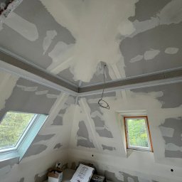 MATEUSZ MOTOR - Poddasze w Skawie w trakcie prac wykończeniowych, ściany i skosy pokryte częściowo nałożoną warstwą szpachli, widoczne okna dachowe i elementy konstrukcyjne.