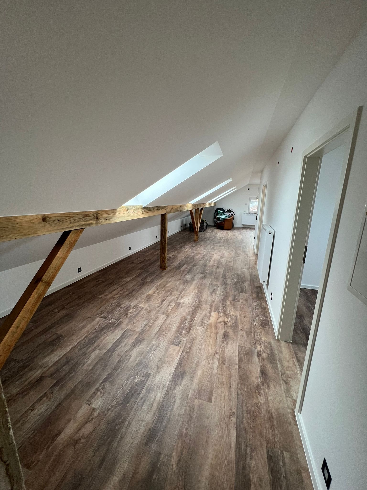 Poddasze po remoncie z drewnianą podłogą imitującą panele, białymi ścianami, drewnianą belką konstrukcyjną i oknami dachowymi.