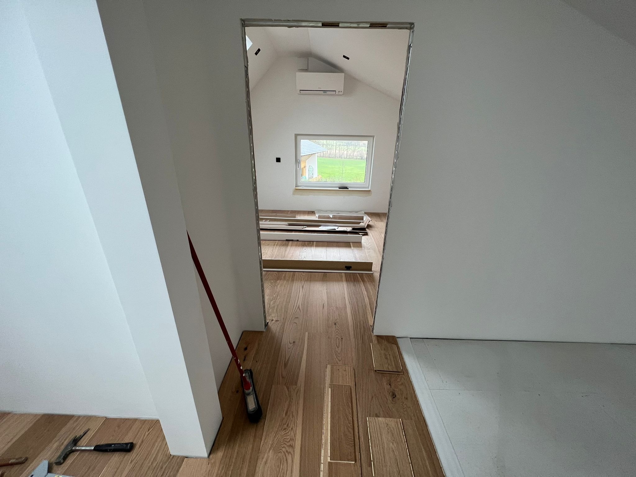 Montaż drewnianej podłogi w pokoju na poddaszu, widoczne narzędzia i deski parkietu, surowe ściany przygotowane do dalszych prac wykończeniowych.