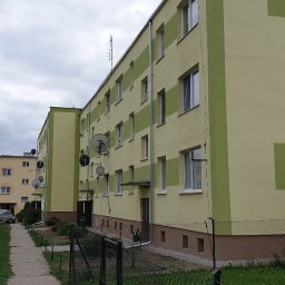 Norbert Gołombiewski BudNext - Blok mieszkalny po remoncie elewacji, z zielonymi pasami dekoracyjnymi, widoczne anteny satelitarne i chodnik.