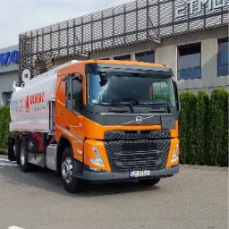 Pomarańczowa cysterna Volvo firmy Olbenz z napisem 'Twój dostawca paliw' na tle budynku firmy ETMU.