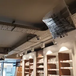 Montaż oświetlenia szynowego i kamery monitoringu w nowym sklepie, widoczne koryta kablowe pod sufitem i regały sklepowe.