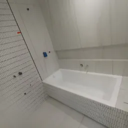 Biała wanna obudowana mozaiką w łazience z białymi płytkami, widoczne otwory na armaturę w ścianie.