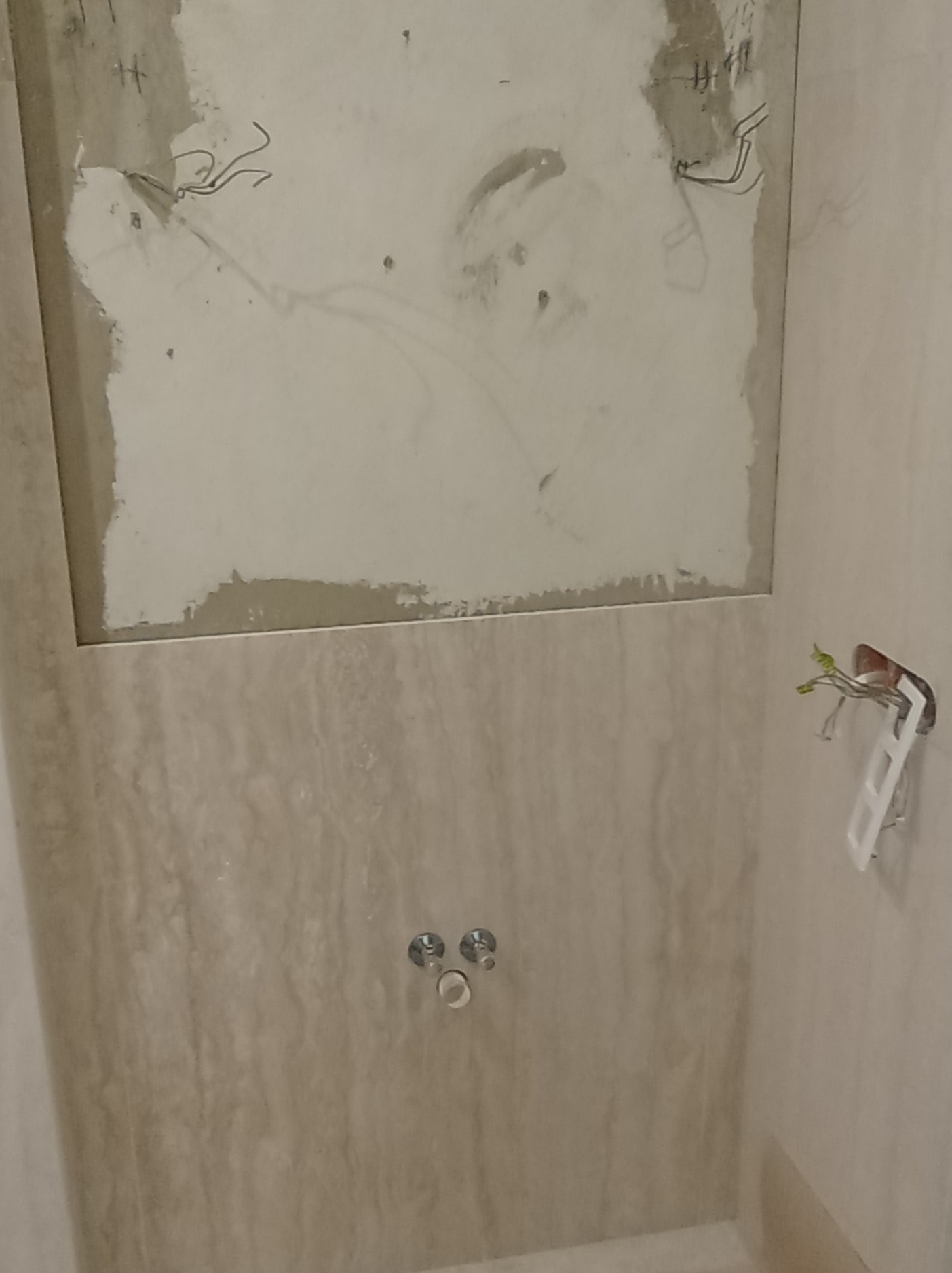 Ściana w łazience w trakcie remontu: częściowo położone płytki imitujące marmur, odsłonięty fragment ściany z instalacją elektryczną i hydrauliczną.