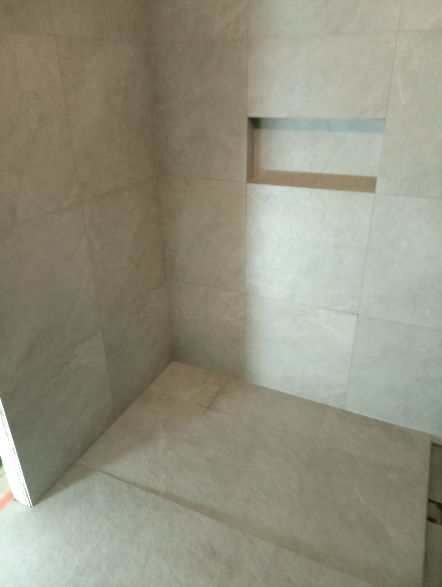 Wykończona wnęka prysznicowa z szarymi płytkami imitującymi kamień, z wbudowaną półką w ścianie.