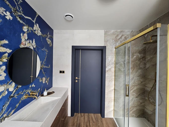 Nowoczesna łazienka z akcentem artystycznym: ściana z motywem kwitnących gałęzi migdałowca Van Gogha, okrągłe lustro, minimalistyczna umywalka z drewnianą szafką, kabina prysznicowa z złotymi...