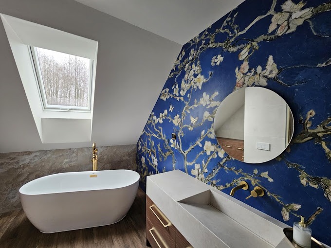 Nowoczesna łazienka na poddaszu z wolnostojącą białą wanną, złotą armaturą i ścianą z motywem kwitnących migdałowców Van Gogha, okrągłe lustro.