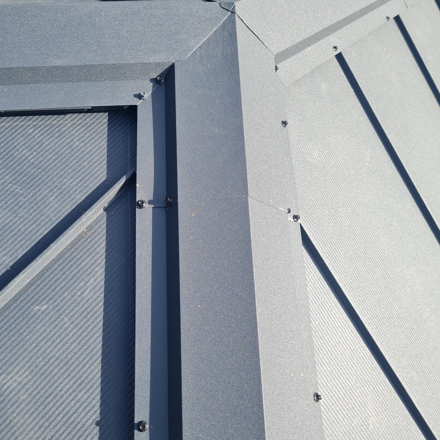 Szczegółowe ujęcie fragmentu dachu z metalu w odcieniach szarości, z widocznymi śrubami mocującymi i liniami cieni, ukazujące precyzję wykonania.