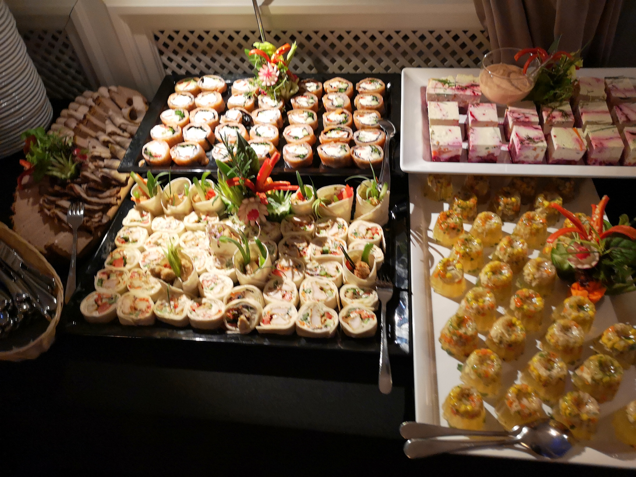 Elegancki bufet z różnorodnymi przekąskami: roladki z tortilli, mini-kanapeczki w galarecie, koreczki i plastry mięs, dekorowane ziołami i warzywami.