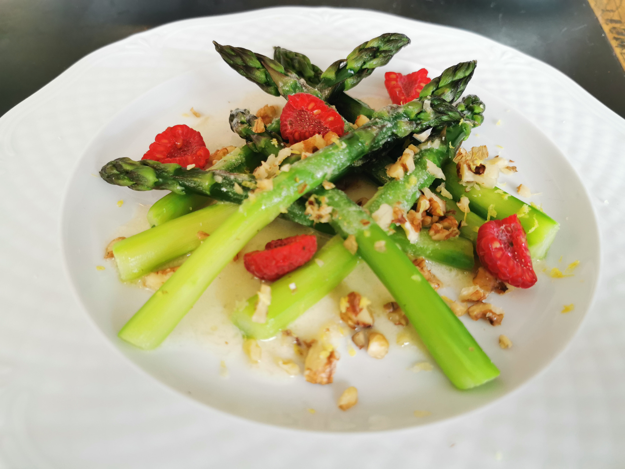 Delikatna kompozycja z zielonych szparagów, malin i orzechów włoskich na białym talerzu, polana sosem.