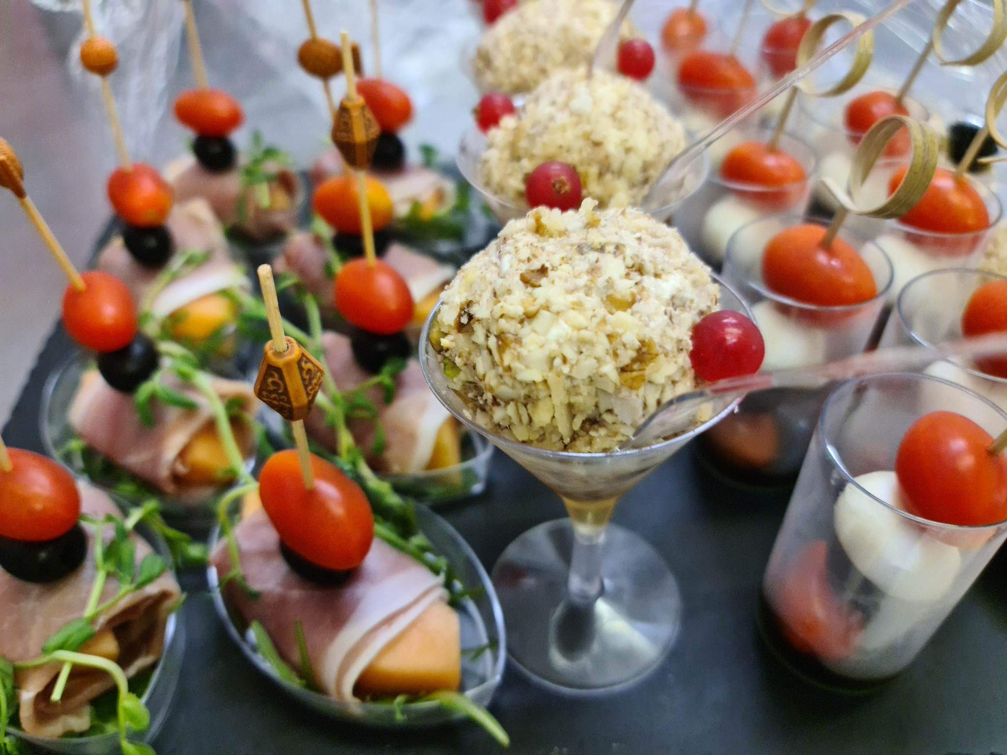 Ekskluzywne przekąski na czarnym talerzu: roladki z szynki z melonem i mikro-ziołami, kulki serowe w orzechowej panierce w kieliszkach koktajlowych oraz mini-szaszłyki z mozzarelli i pomidorków...