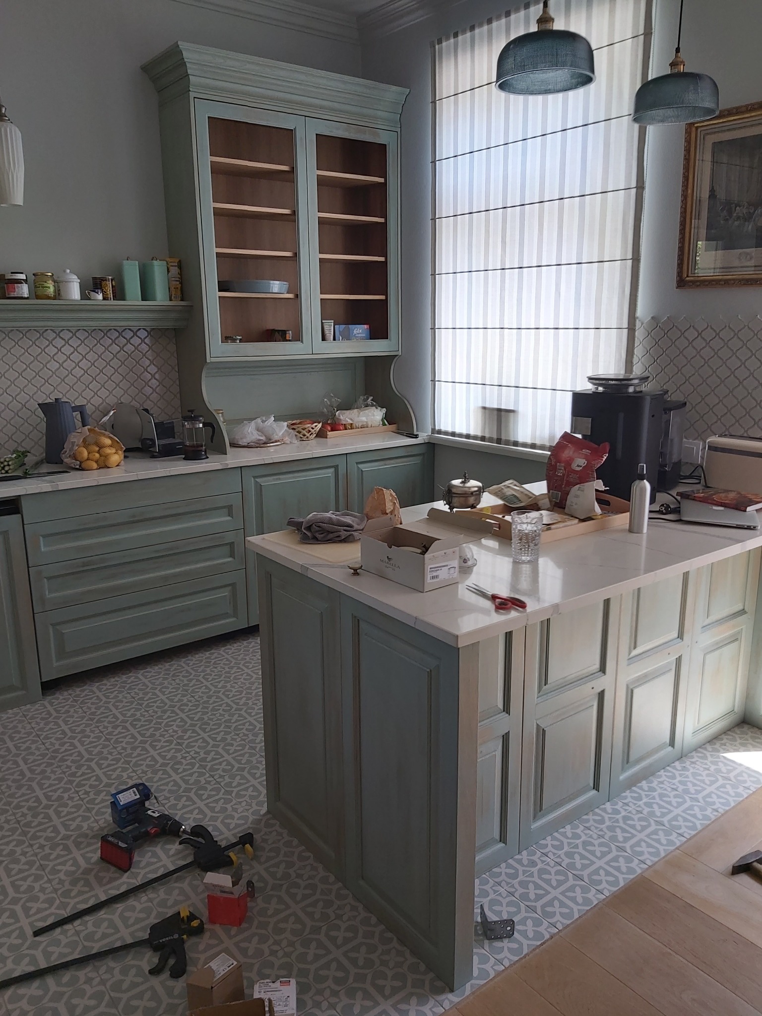 Wnętrze kuchni w stylu rustykalnym z niebieskimi szafkami, wyspą i narzędziami na podłodze w trakcie montażu.