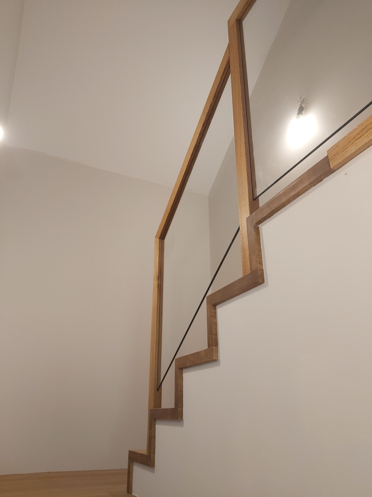 Nowoczesne schody z drewnianą konstrukcją i szklaną balustradą w Sobkowie, z widocznym oświetleniem sufitowym.