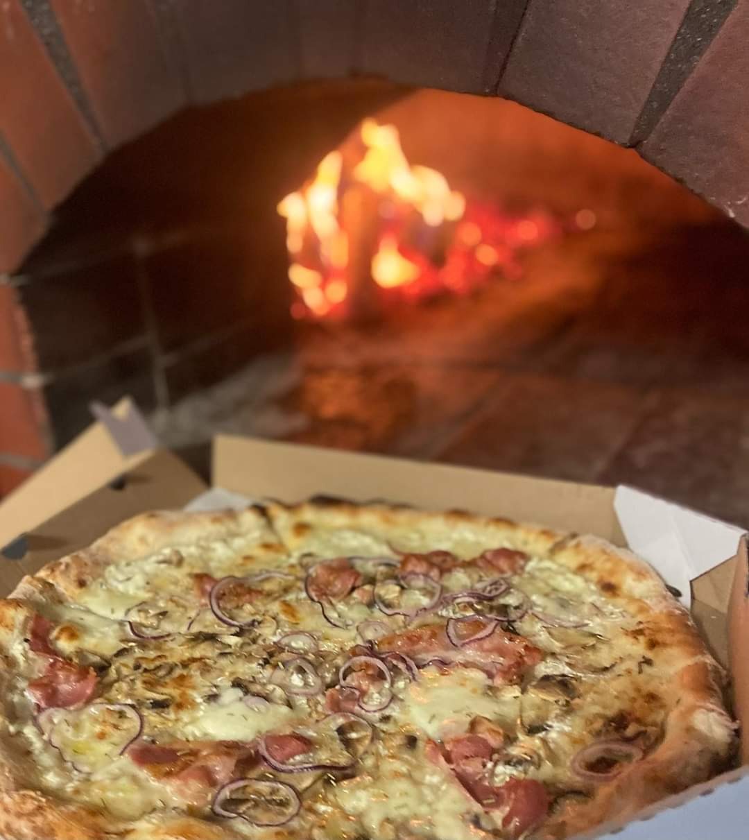 Pizza z pieca opalanego drewnem, w kartonie, z szynką, pieczarkami i czerwoną cebulą na kremowym sosie.