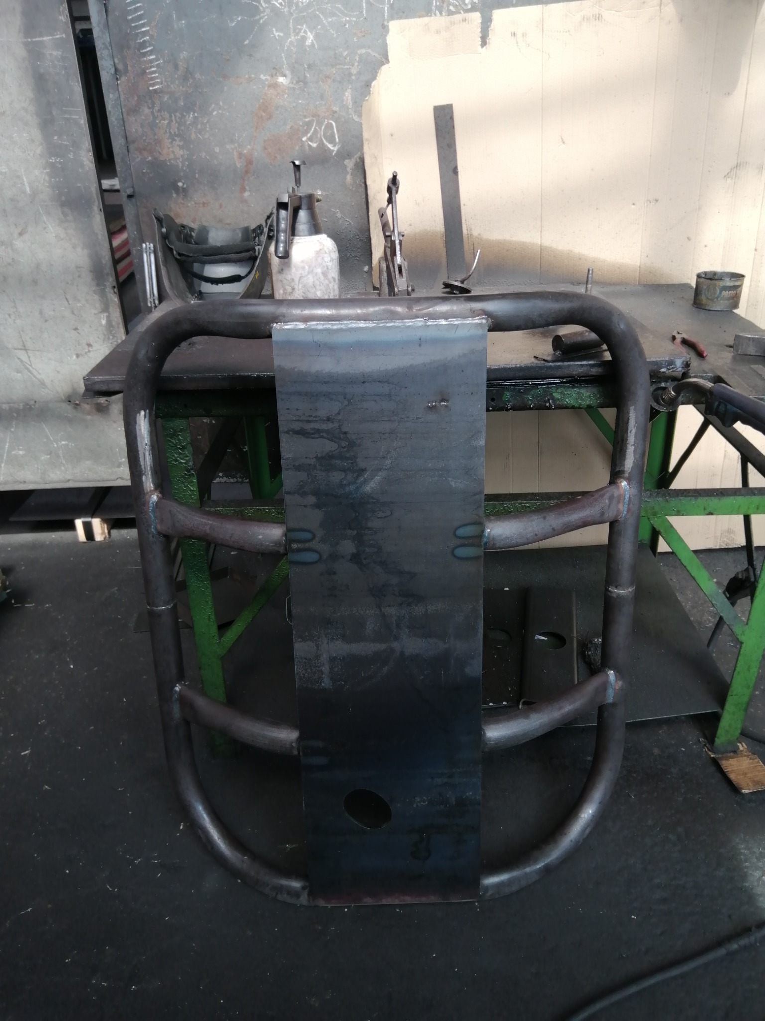 Metalowa konstrukcja z rur i blachy, spawana, umieszczona na warsztatowym stole, widoczne ślady spawania i obróbki metalu, w tle narzędzia i osprzęt spawalniczy.