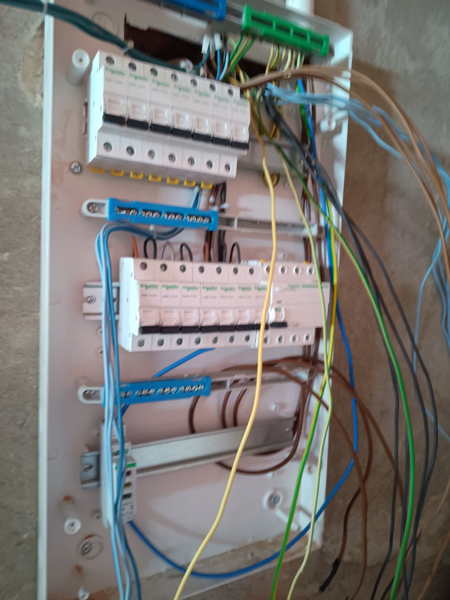 Otwarta skrzynka elektryczna z widocznymi bezpiecznikami i różnokolorowymi przewodami na tle surowej ściany.