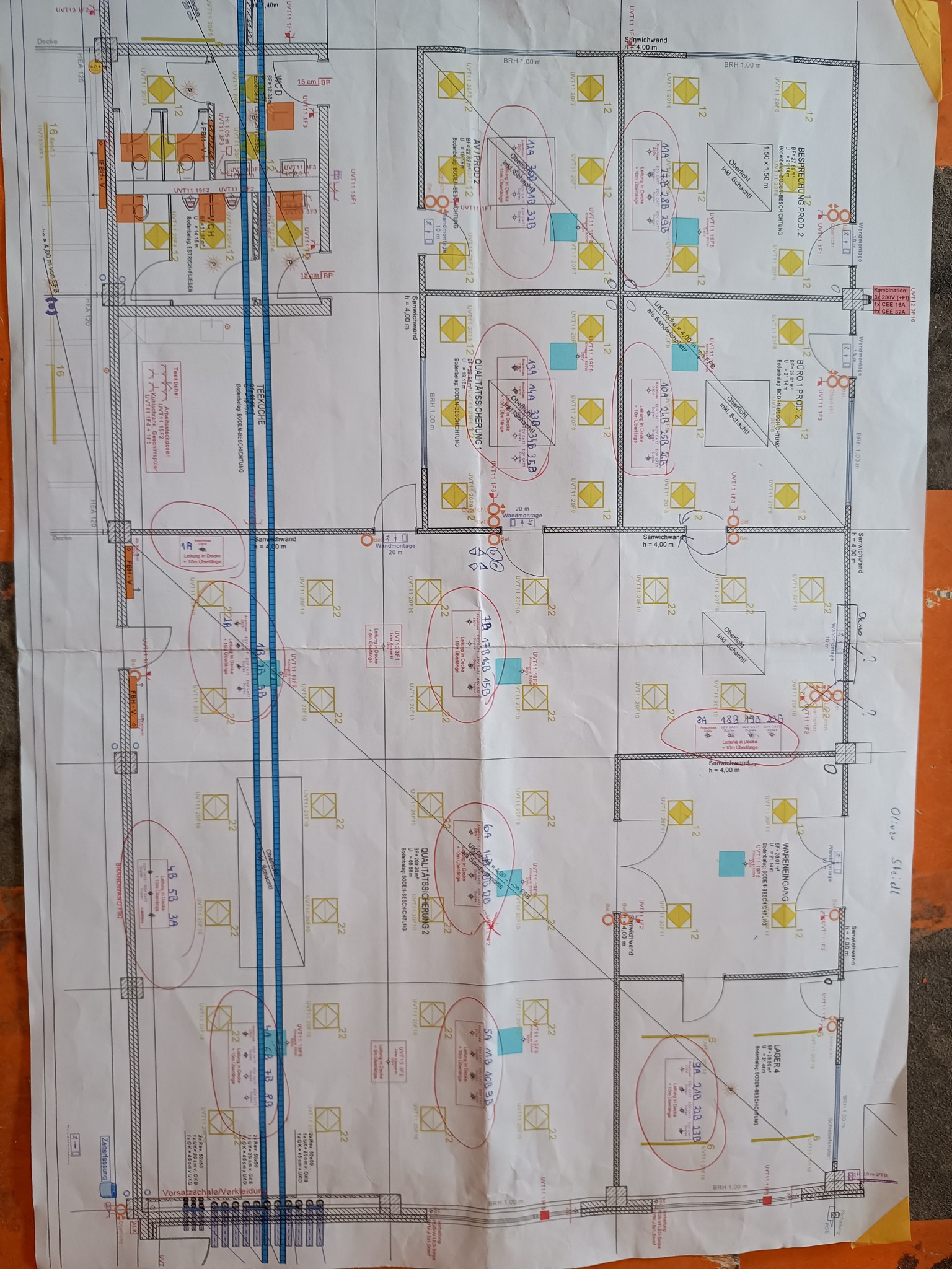 Plan instalacji elektrycznej biura z zaznaczonymi punktami oświetleniowymi i gniazdkami nałożony na kartkę papieru A3, z naniesionymi odręcznymi notatkami w kolorze czerwonym.