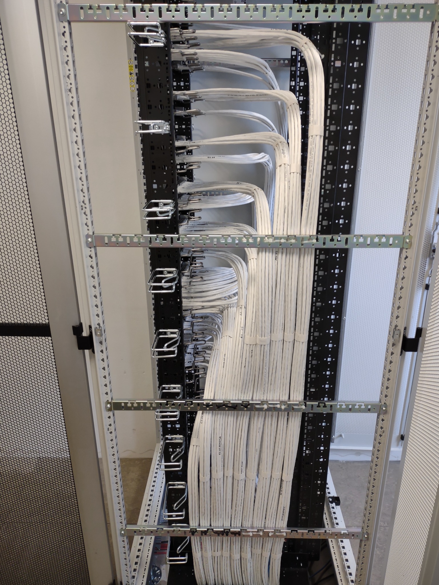 Rząd białych kabli sieciowych starannie ułożonych w metalowej szafie rack, z widocznymi uchwytami i perforowanymi panelami bocznymi.