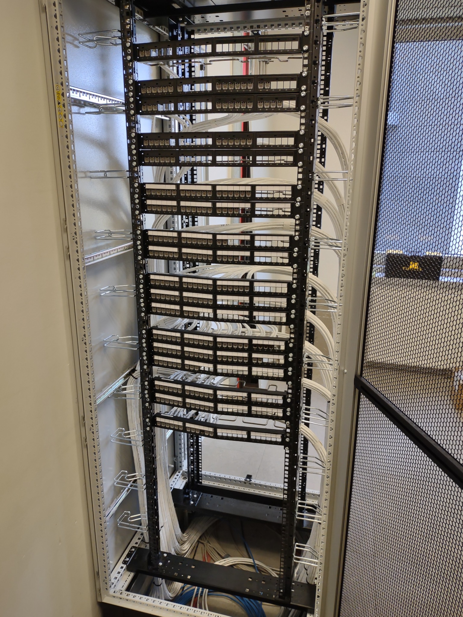 Panel krosowniczy z uporządkowanymi kablami sieciowymi w szafie rack, widoczne metalowe uchwyty do prowadzenia kabli.