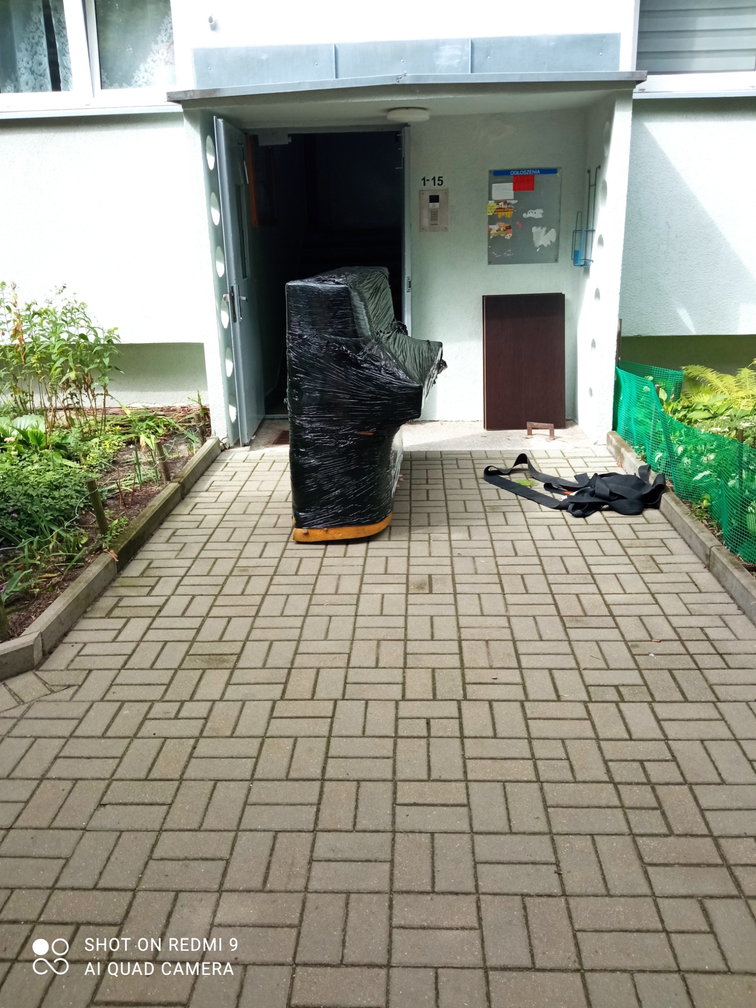 Pianino owinięte folią stretch przygotowane do transportu przed budynkiem w Łodzi, widoczne pasy transportowe.