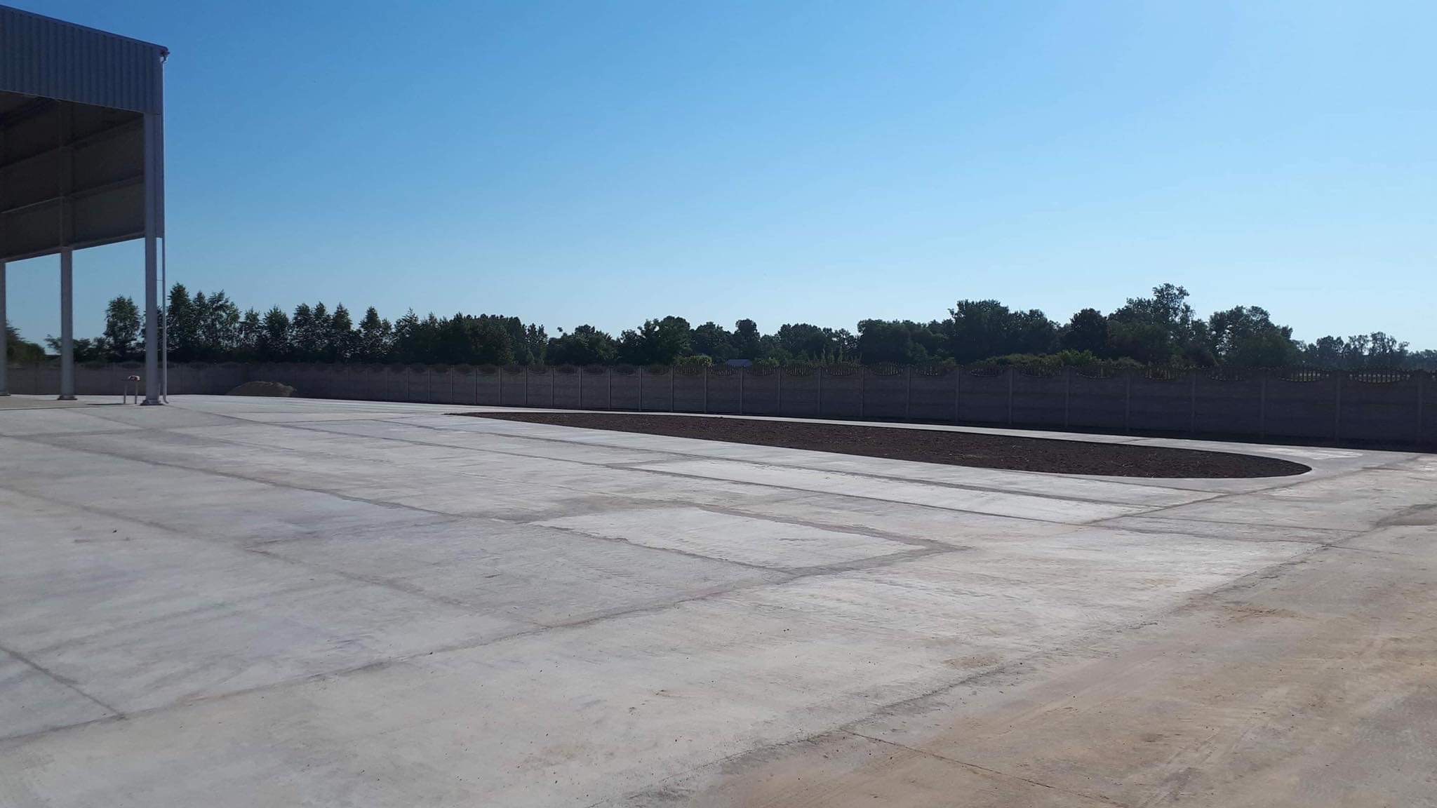 Nowa, betonowa nawierzchnia placu z przygotowanym miejscem pod nasadzenia wzdłuż ogrodzenia z prefabrykatów betonowych.