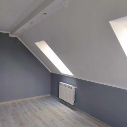 PRO-BUD Przemysław Wrzesniewski - Pokój na poddaszu po remoncie: szare ściany, biały grzejnik, jasne panele podłogowe, okno dachowe i otwory na oświetlenie sufitowe z wystającymi kablami.