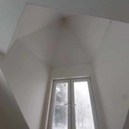 PRO-BUD Przemysław Wrzesniewski - Wnętrze pokoju na poddaszu z oknem, ściany i sufit świeżo pomalowane na biało, widoczne ślady po niedoskonałościach na suficie, za oknem zima.