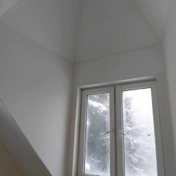 PRO-BUD Przemysław Wrzesniewski - Świeżo pomalowane na biało wnętrze pokoju z oknem, widoczne ślady po taśmie malarskiej na parapecie, z zewnątrz widok zaśnieżonych drzew.