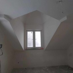 PRO-BUD Przemysław Wrzesniewski - Pokój na poddaszu po malowaniu na biało, widoczne okno z widokiem na drzewa i niedoskonałości na podłodze.