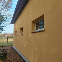 PRO-BUD Przemysław Wrzesniewski - Ocieplona i pomalowana na żółto elewacja domu jednorodzinnego w Lipnie, widoczne trzy okna i opadłe liście na ziemi.