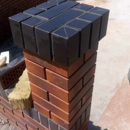 PRO-BUD Przemysław Wrzesniewski - Murowany słupek z cegły klinkierowej, zwieńczony czarnymi, błyszczącymi elementami z betonu architektonicznego, w trakcie budowy ogrodzenia.