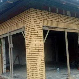 PRO-BUD Przemysław Wrzesniewski - Budynek w trakcie wykańczania elewacji z żółtej cegły klinkierowej, widoczne podpory drewniane i niedokończone ściany z czerwonej cegły.