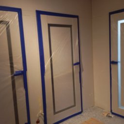 PRO-BUD Przemysław Wrzesniewski - Przygotowanie do malowania: trzy drzwi zabezpieczone folią i niebieską taśmą malarską w rogu pokoju.