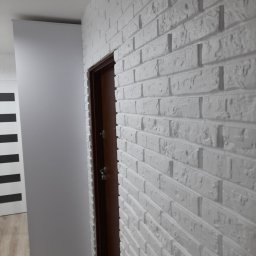 Brak firmy - Ściana z białej cegły dekoracyjnej z brązowymi drzwiami i fragmentem drugiej ściany w tle.