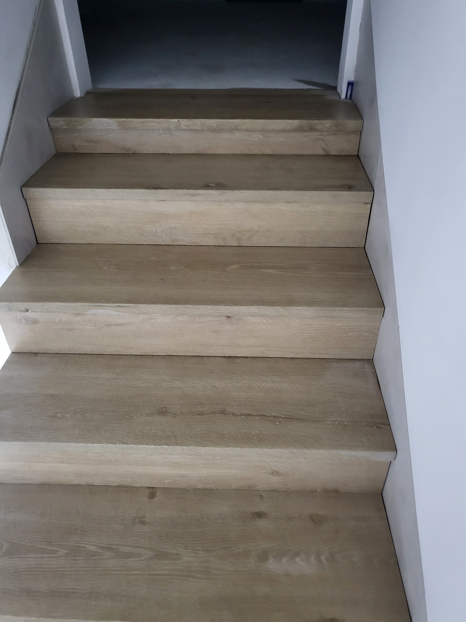 Schody wewnętrzne wykończone panelami imitującymi jasne drewno, widok z dołu, minimalistyczne białe ściany.