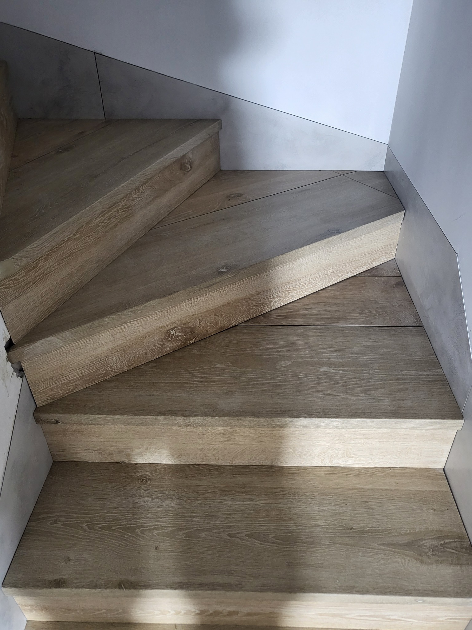 Schody wykończone panelami drewnopodobnymi, z płytkami ceramicznymi na ścianie i podstopnicach.