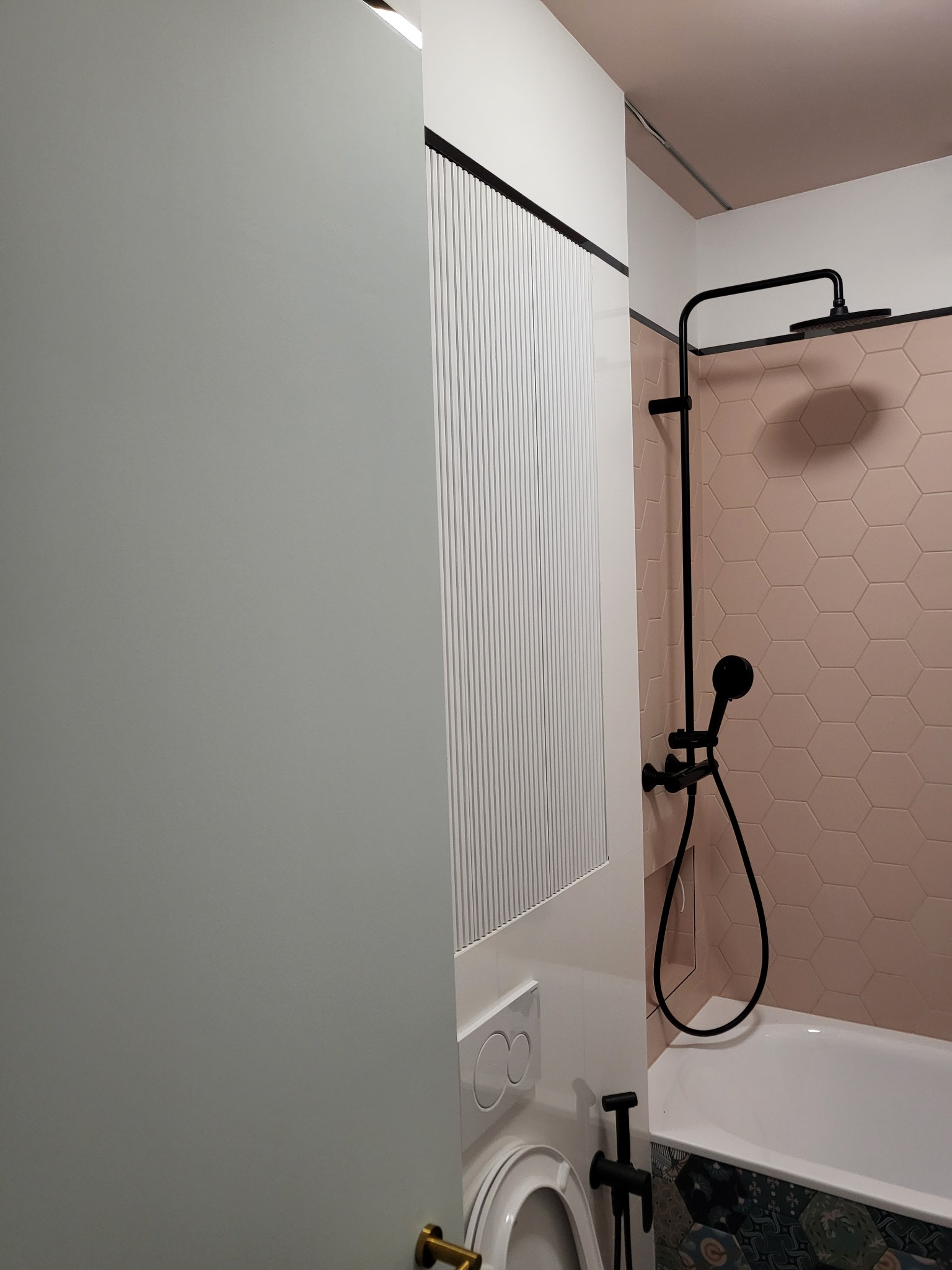 Nowoczesna łazienka z różowymi heksagonalnymi płytkami, czarną armaturą i zabudową z pionowymi lamelami.