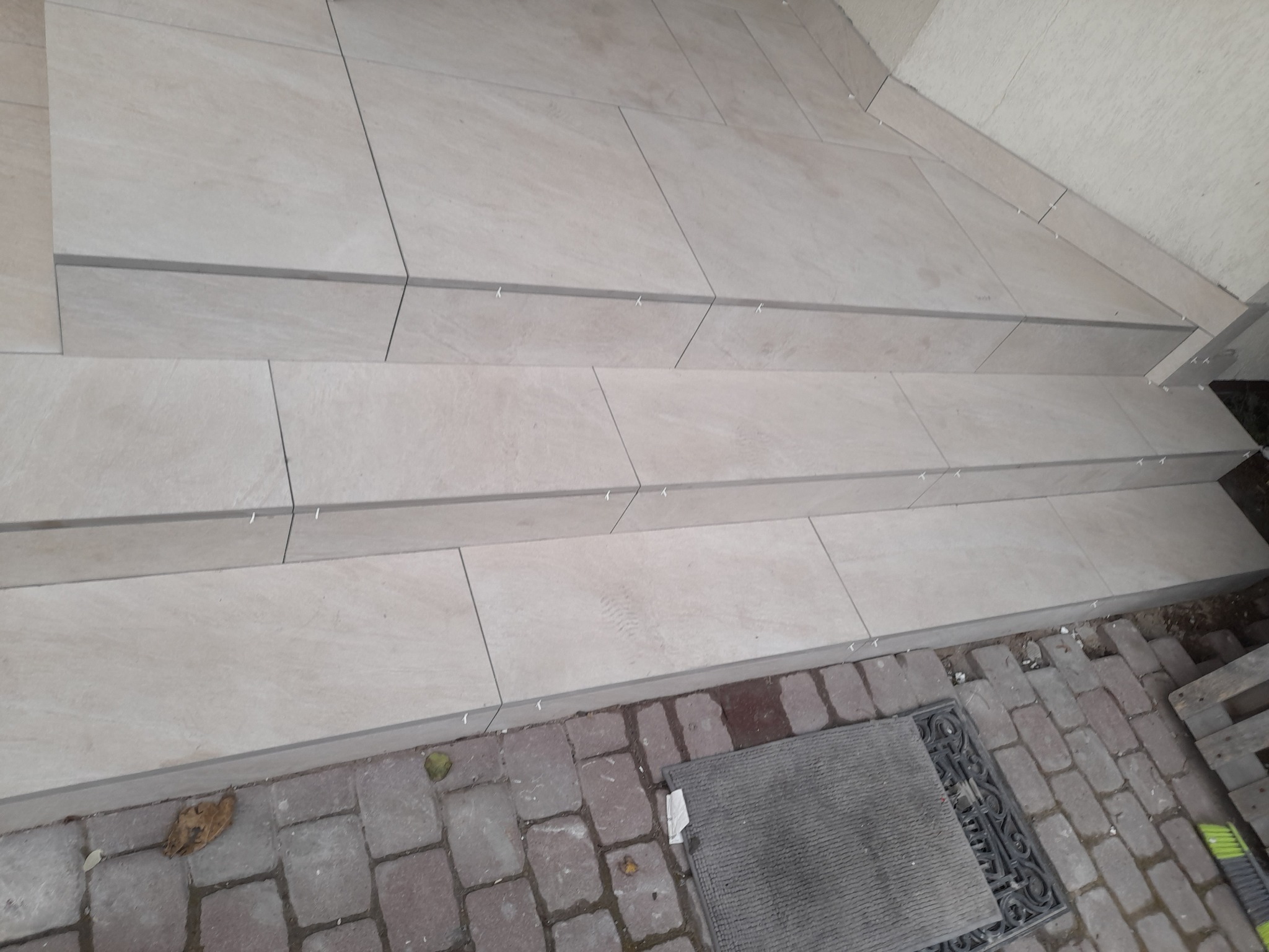 Wyłożone jasnymi płytkami schody zewnętrzne z plastikowymi krzyżykami dystansowymi w spoinach, widok z góry pod kątem.