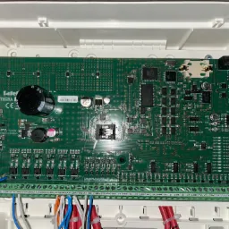 Wnętrze centrali alarmowej z widoczną płytą główną, licznymi elementami elektronicznymi i podłączonymi przewodami.
