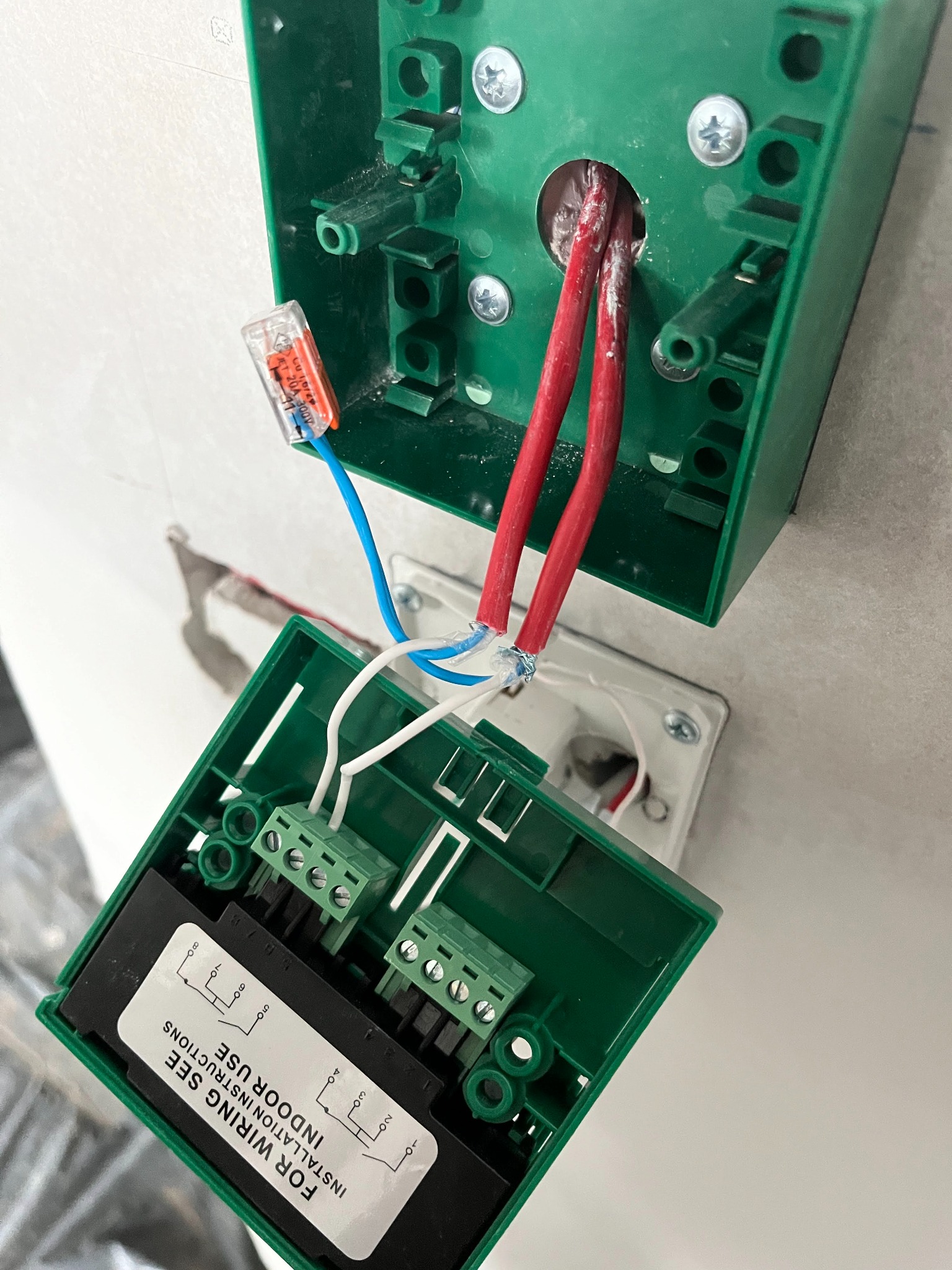 Zielona puszka elektryczna z podłączonymi przewodami: czerwonymi, białymi i niebieskimi, widoczne złącza WAGO, montaż instalacji wewnątrz budynku.