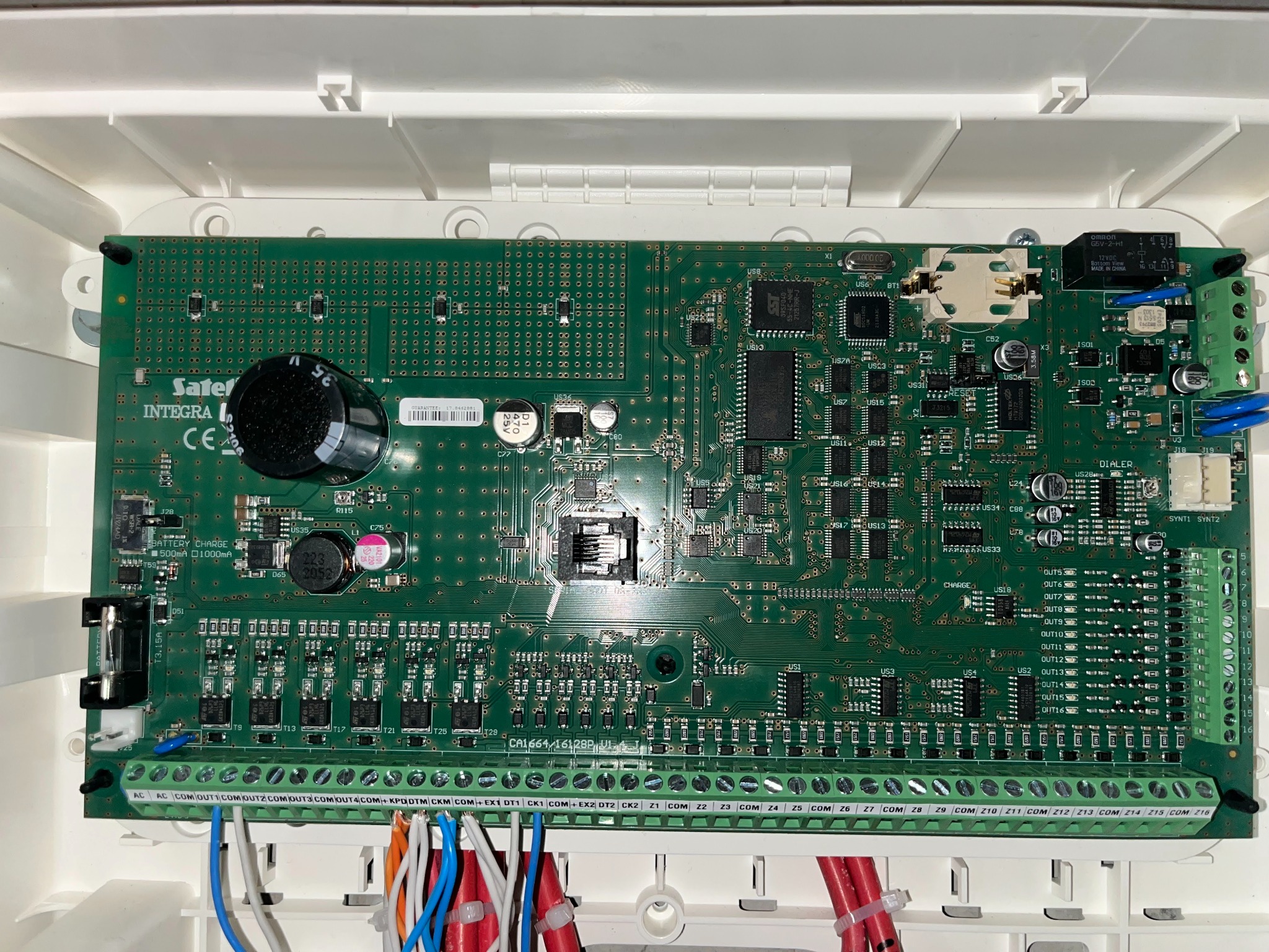 Wnętrze centrali alarmowej z widoczną płytą główną, licznymi elementami elektronicznymi i podłączonymi przewodami.