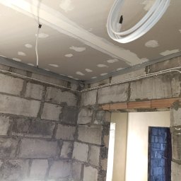 ANdom Instalacje Elektryczne - Świeżo położone, białe przewody elektryczne w nowym budynku z surowymi ścianami z betonu komórkowego i częściowo wykończonym sufitem podwieszanym.