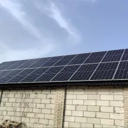 Panele słoneczne zamontowane na dachu budynku z białej cegły, widok z dołu na pochmurne niebo.