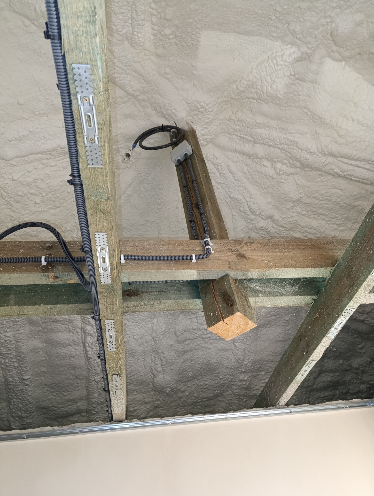 Poddasze ocieplone pianą PUR z widoczną drewnianą konstrukcją dachu, przewodami elektrycznymi w peszlach oraz metalowymi łącznikami.