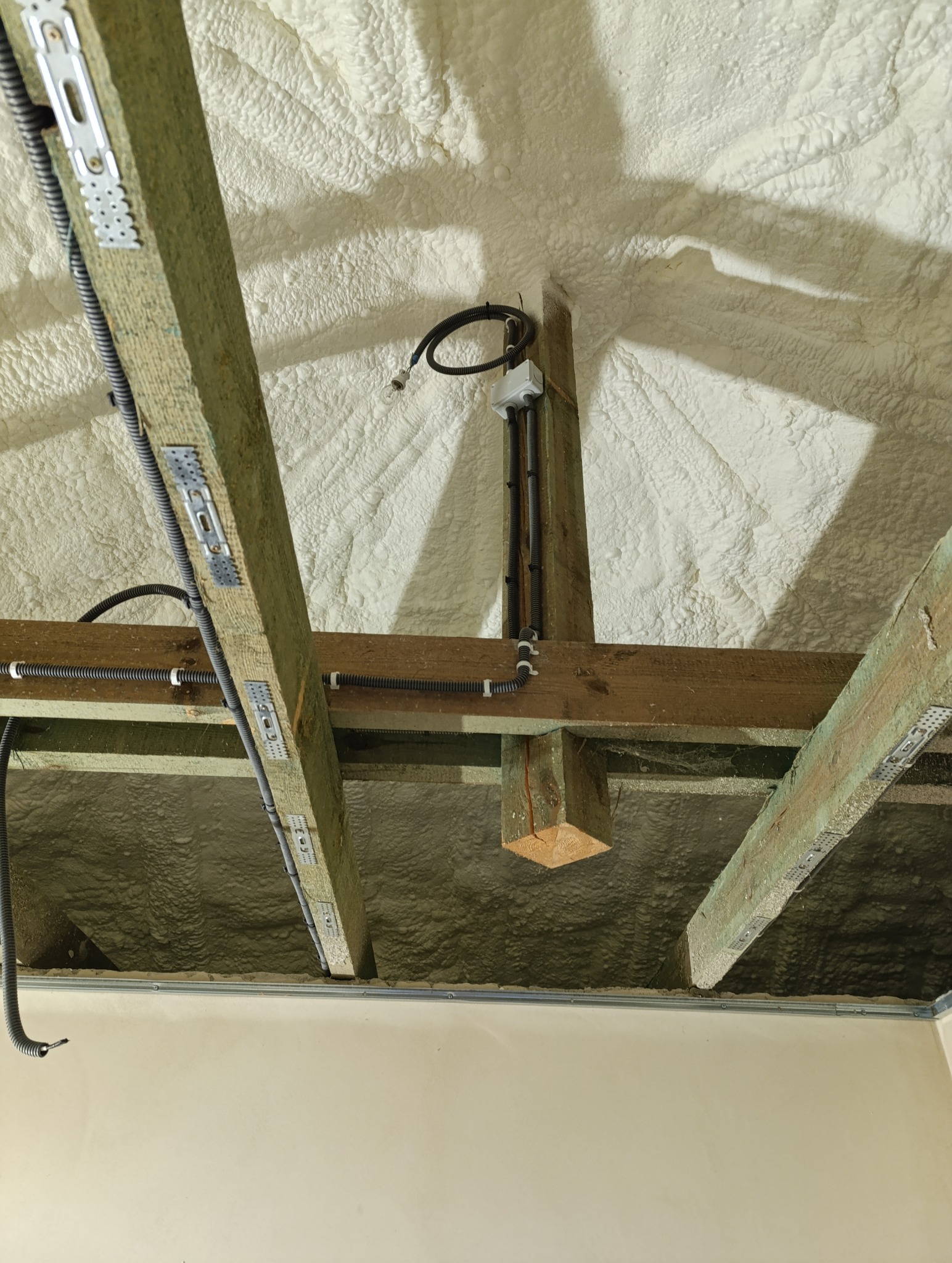 Izolacja poddasza pianką PUR z widocznymi elementami konstrukcji drewnianej i instalacji elektrycznej w peszlach.