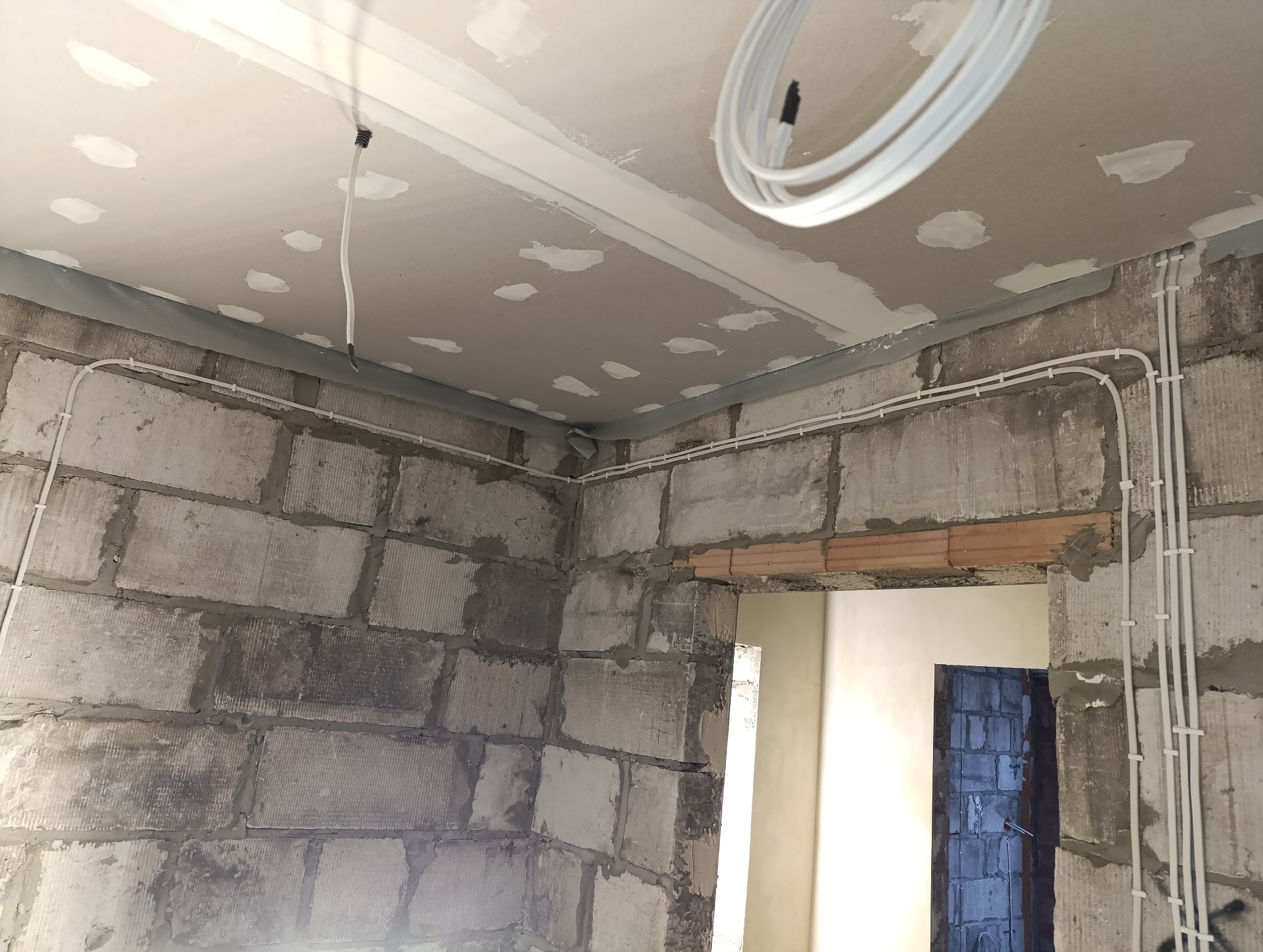 Świeżo położone, białe przewody elektryczne w nowym budynku z surowymi ścianami z betonu komórkowego i częściowo wykończonym sufitem podwieszanym.